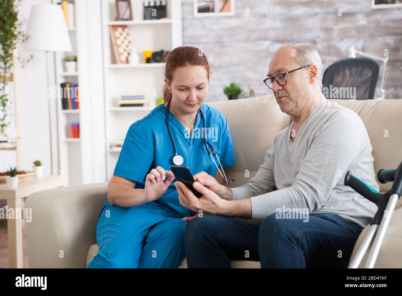 Female doctor in nursing home showing old man how to use mobile phone