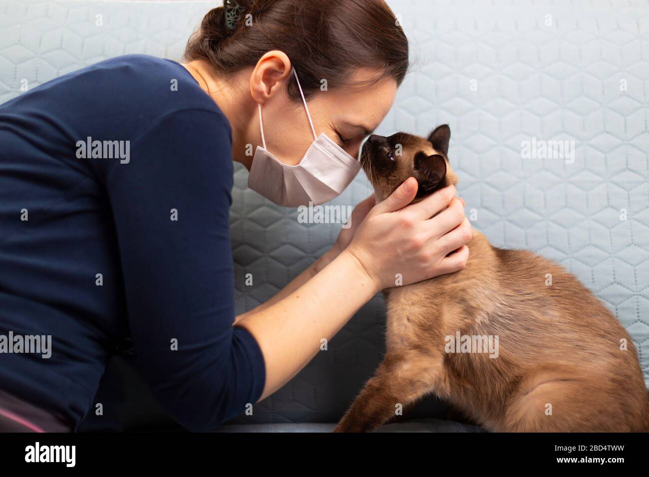 Woman in self isolation mask with her cat having a moment of affection. Isolation and self-quarantine. Stock Photo