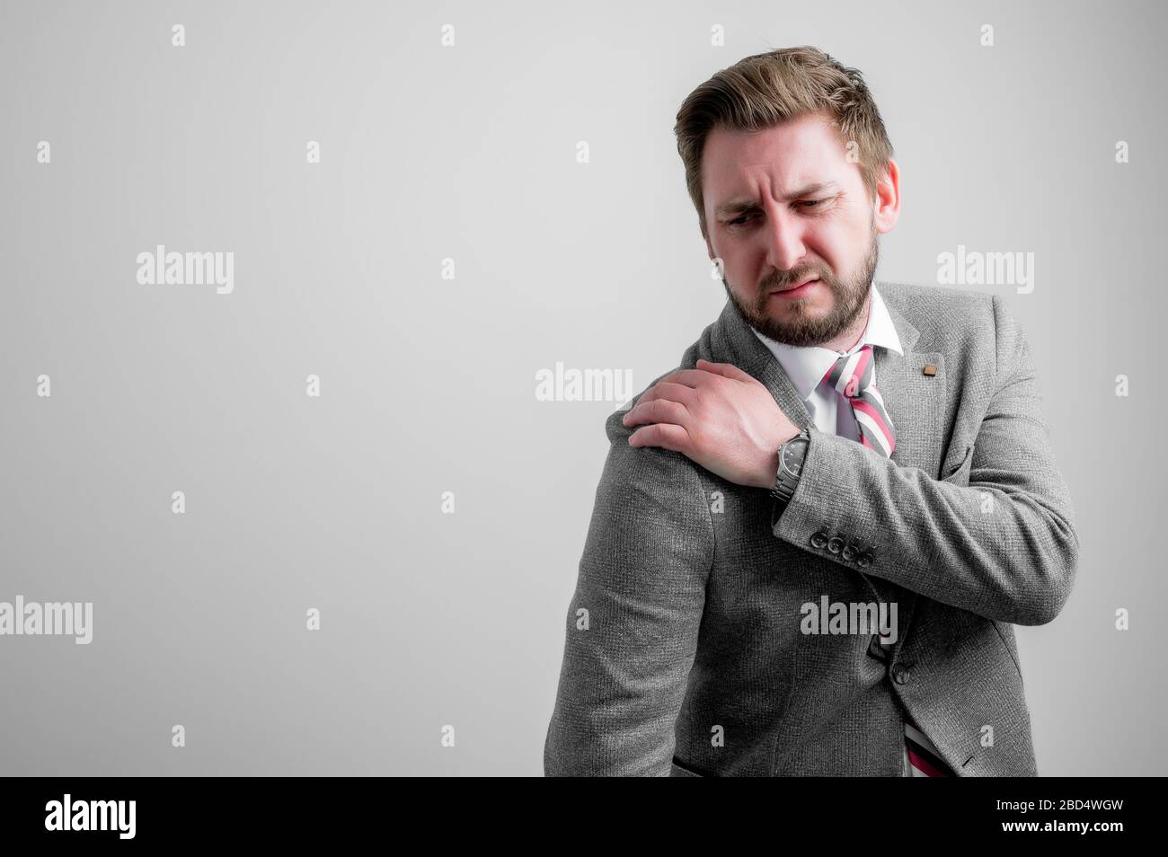 Portrait of business man wearing business clothes gesturing shoulder ache isolated on grey background with copy space advertising area Stock Photo