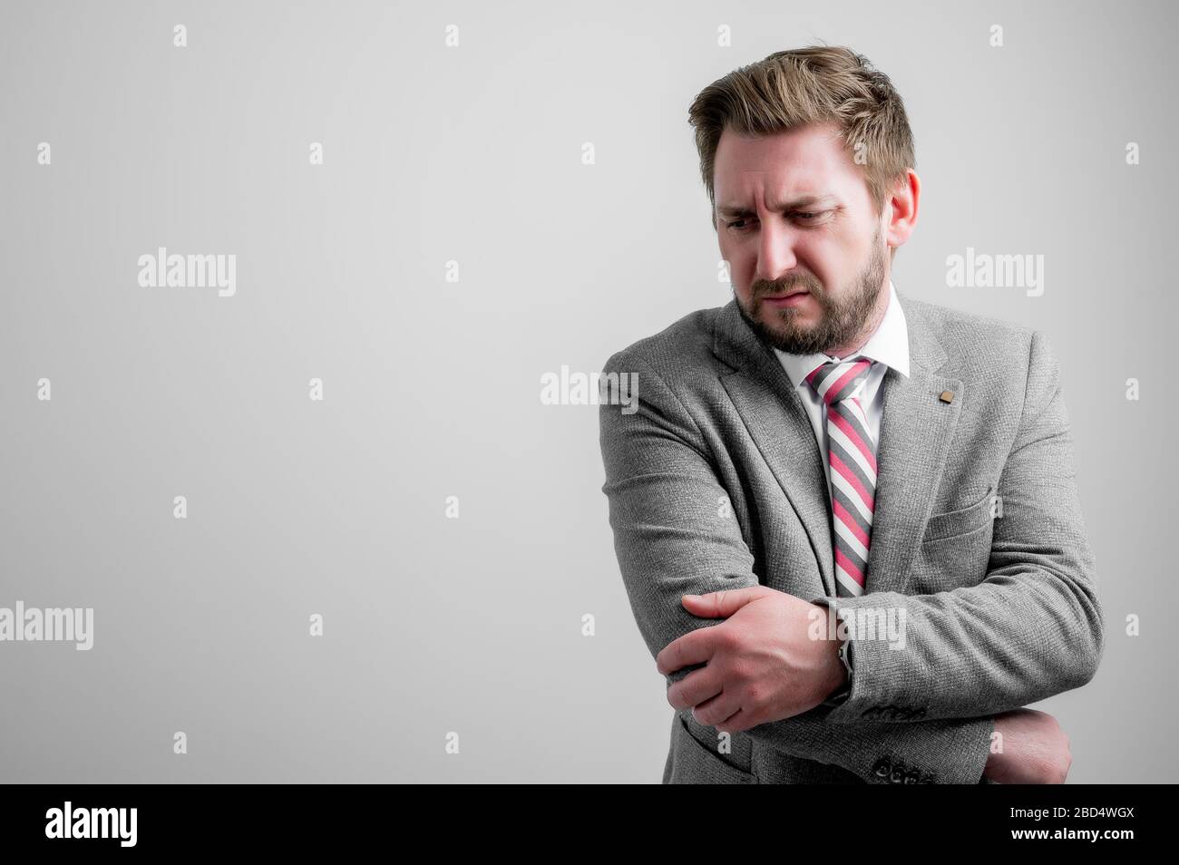 Portrait of business man wearing business clothes gesturing elbow ache isolated on grey background with copy space advertising area Stock Photo