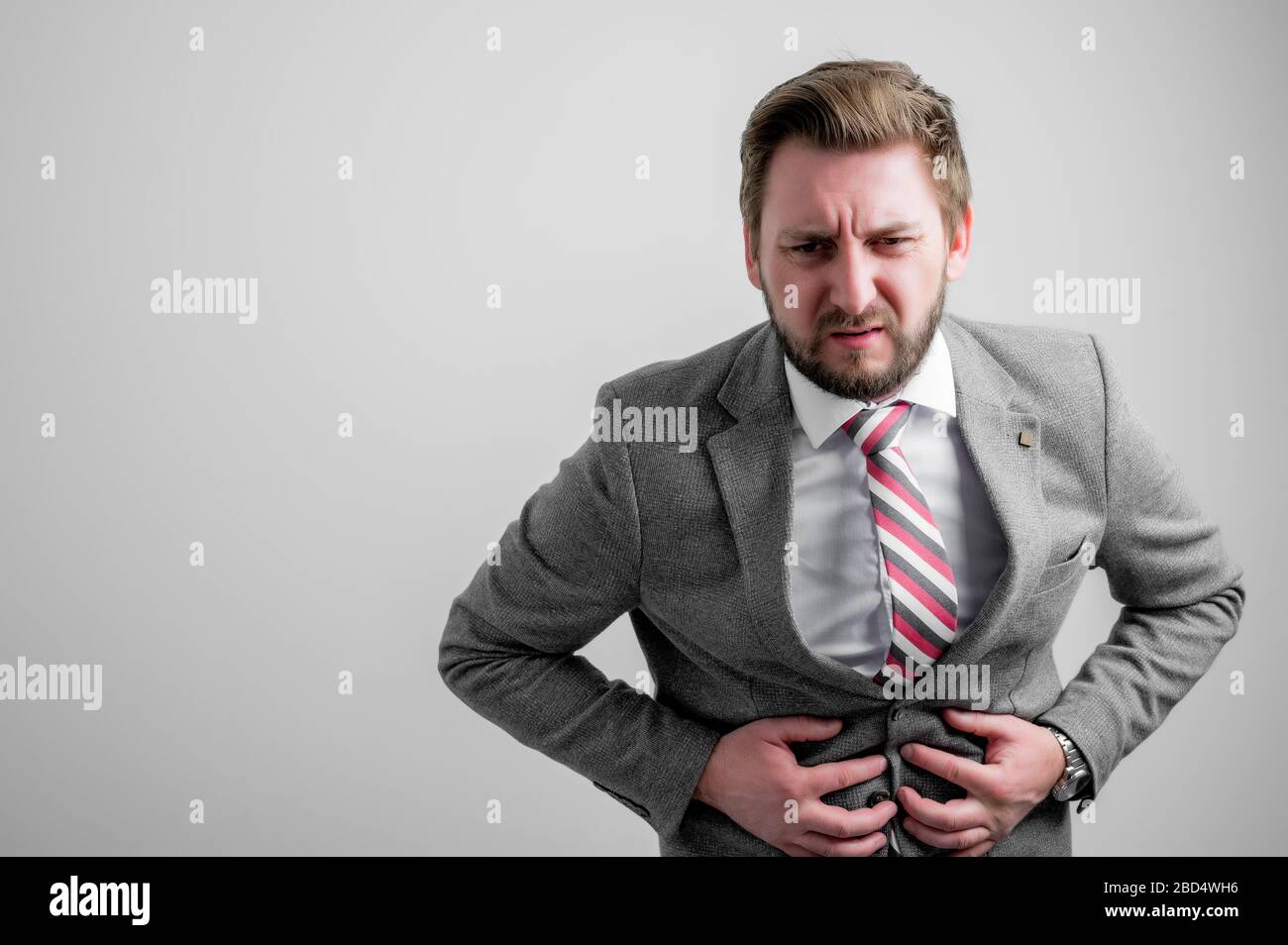 Portrait of business man wearing business clothes gesturing stomach ache isolated on grey background with copy space advertising area Stock Photo