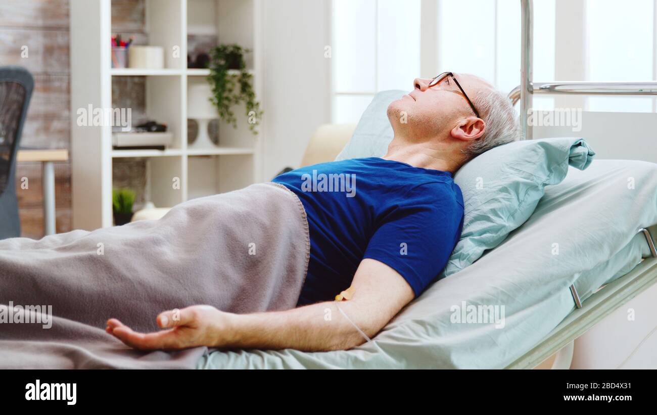 Portrait of elderly sick man lying in hospital bed in a retirement home with a cannula in his