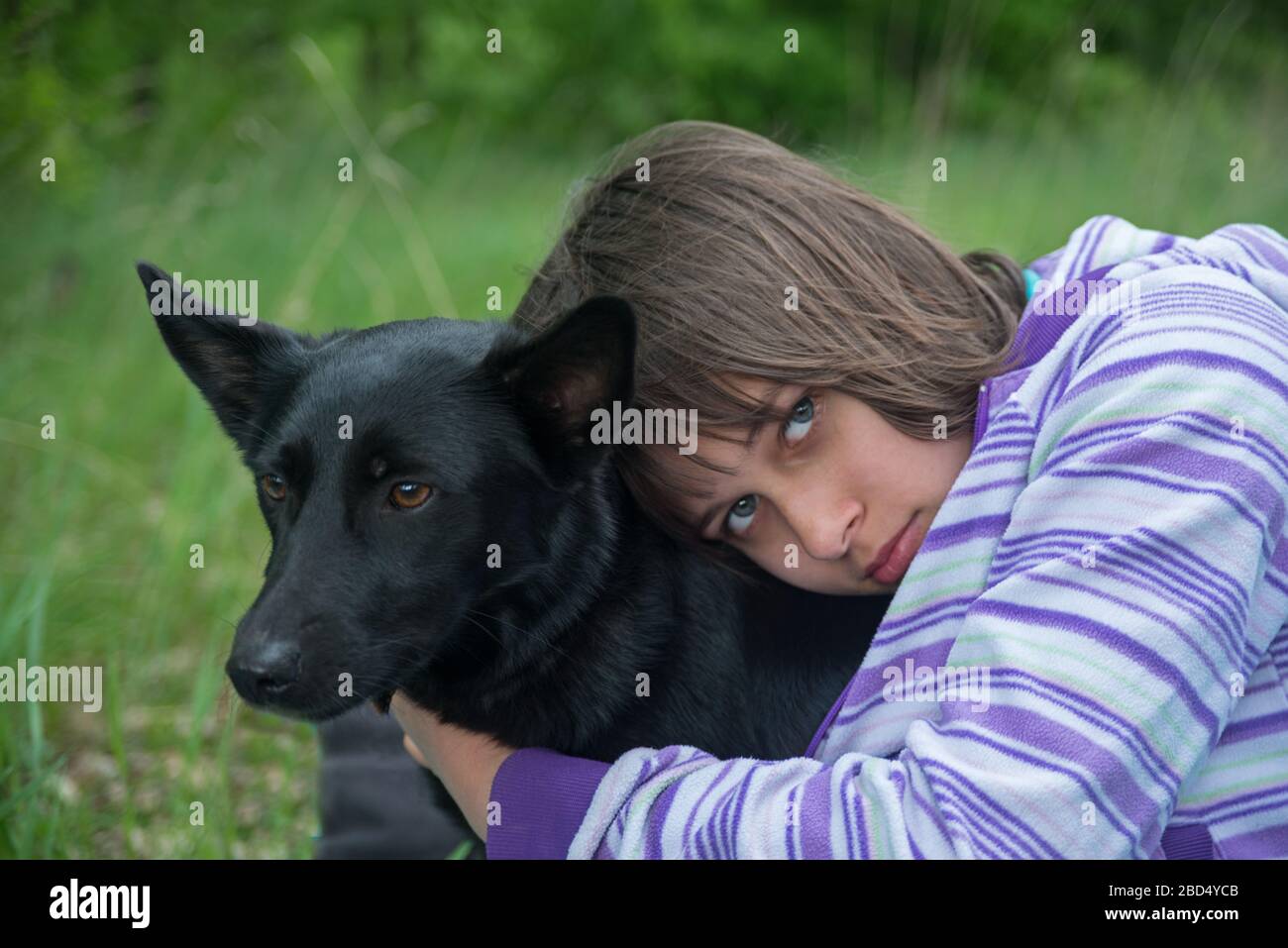 The girl  takes in arms black dog (her pet). Child and animal is situated against natural green background. Stock Photo