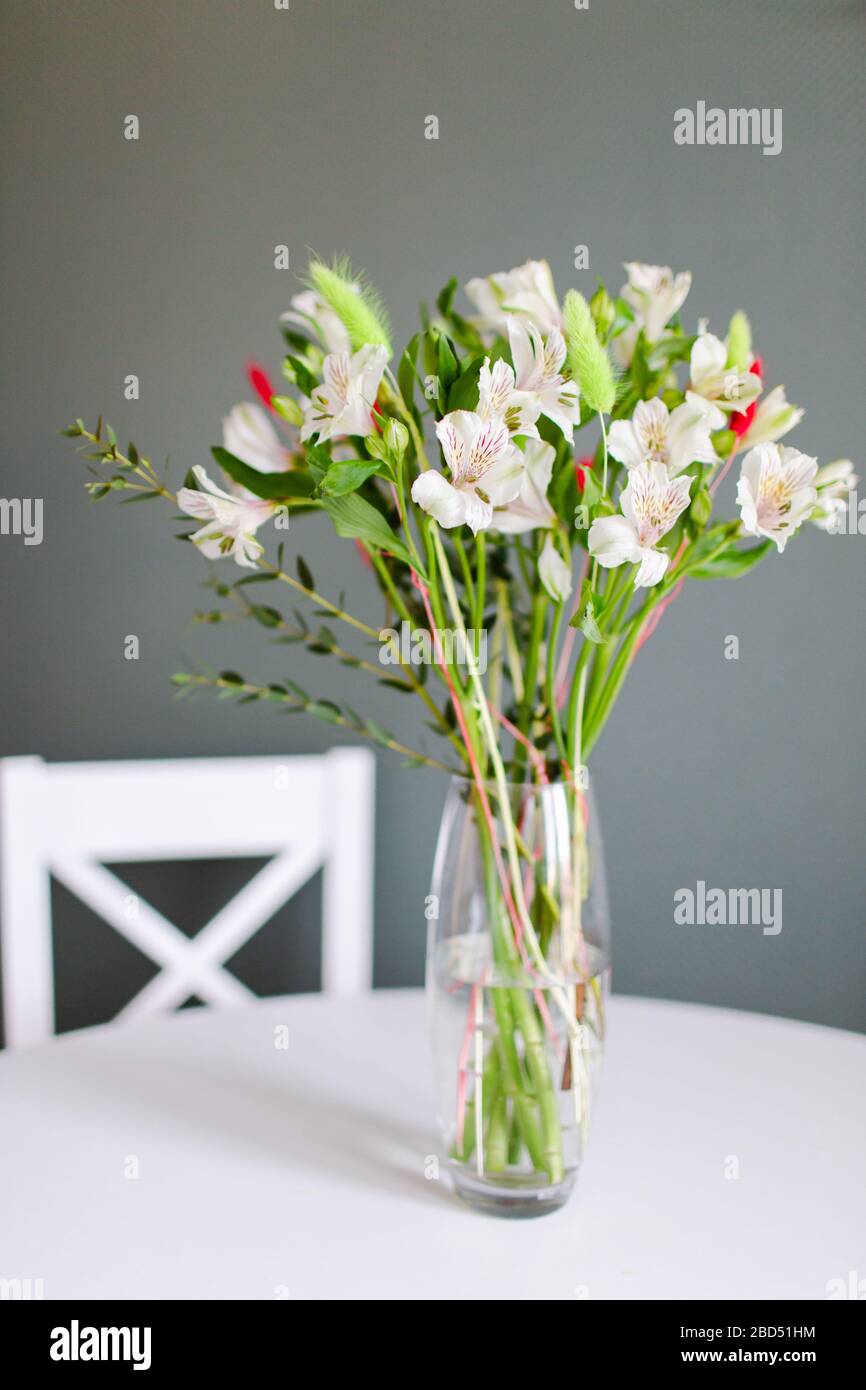 Bouquet of white alstroemeria flowers in clear vase staying on a white round table Stock Photo