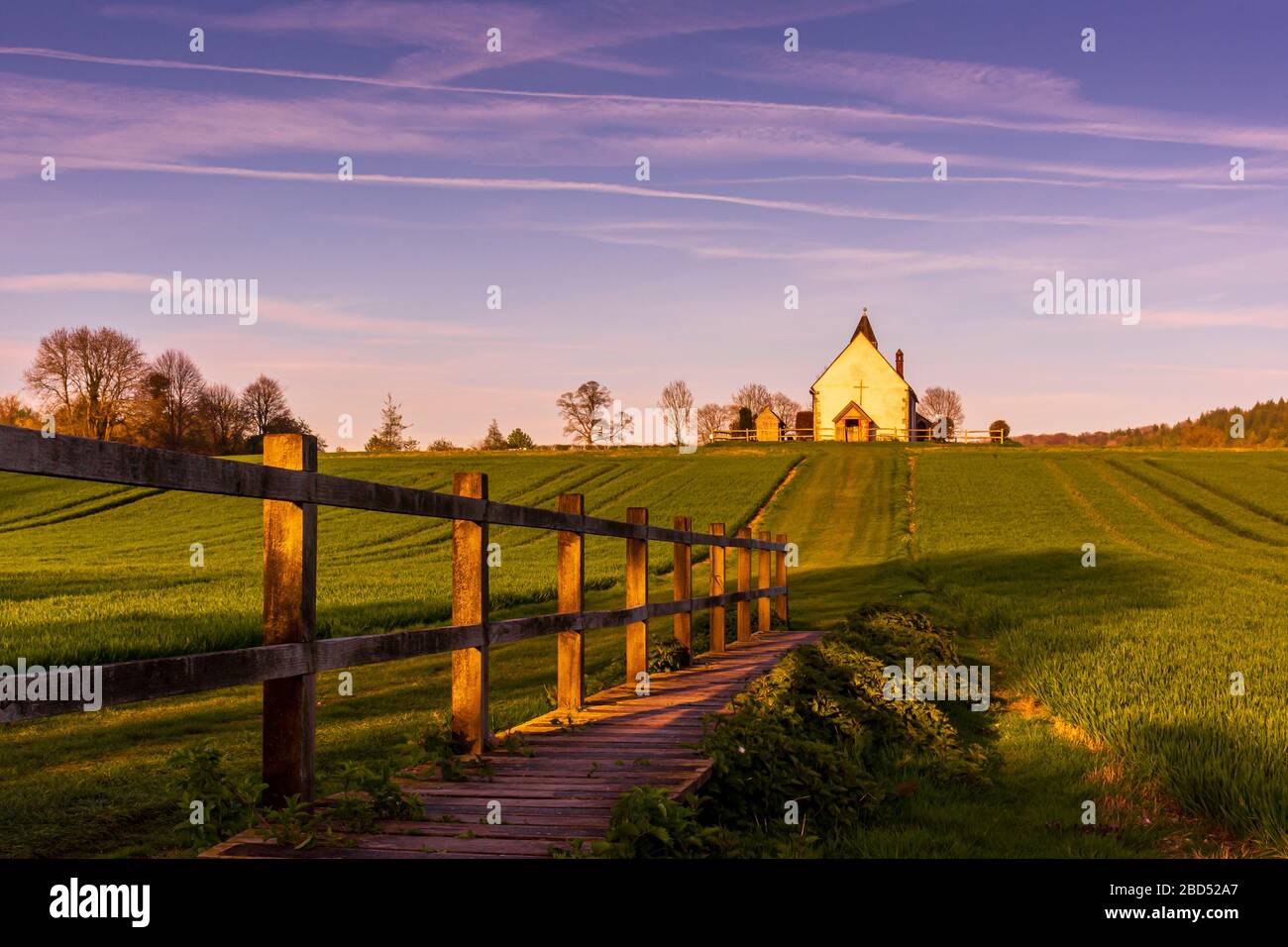 Wooden boardwalk leading to the Isolated St Hubert's Church in a green field, South Downs National Park on a sunny Summer evening during golden hour Stock Photo