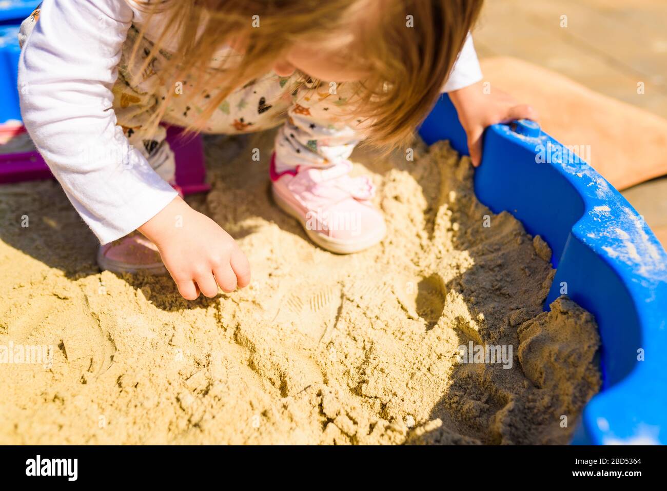 Baby girl playing in a sandbox outdoors in sunny day. Child in blue sandbox in summer. Stock Photo