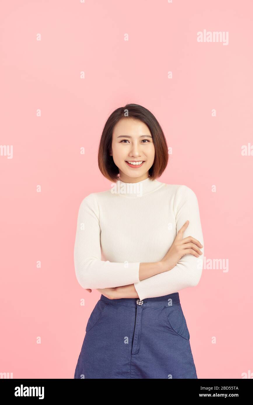 Young Asian woman wearing  sweater standing over isolated pink background happy face smiling with crossed arms looking at the camera. Positive person. Stock Photo