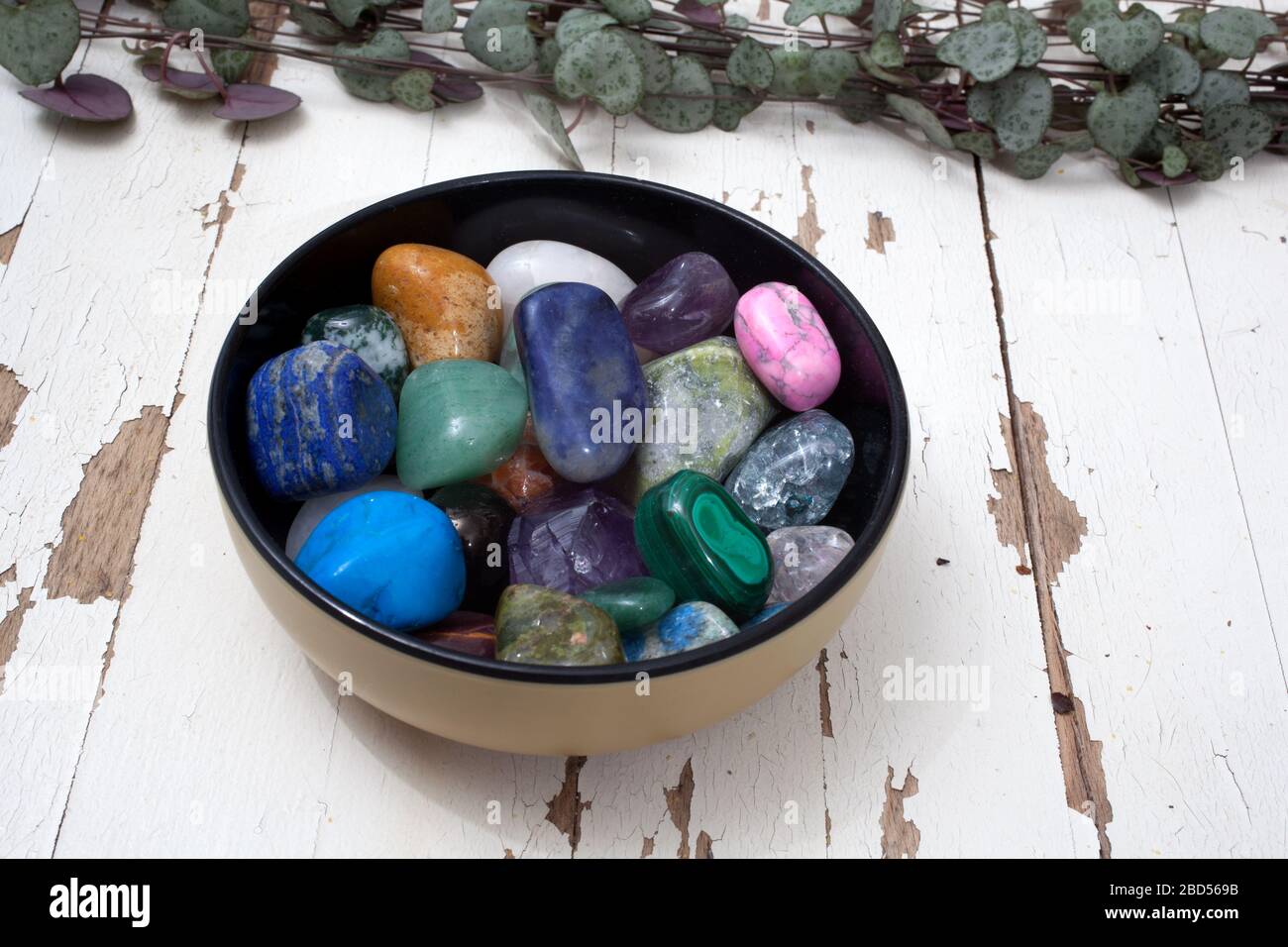 A bowl of assorted gemstones photographed against a white rustic
