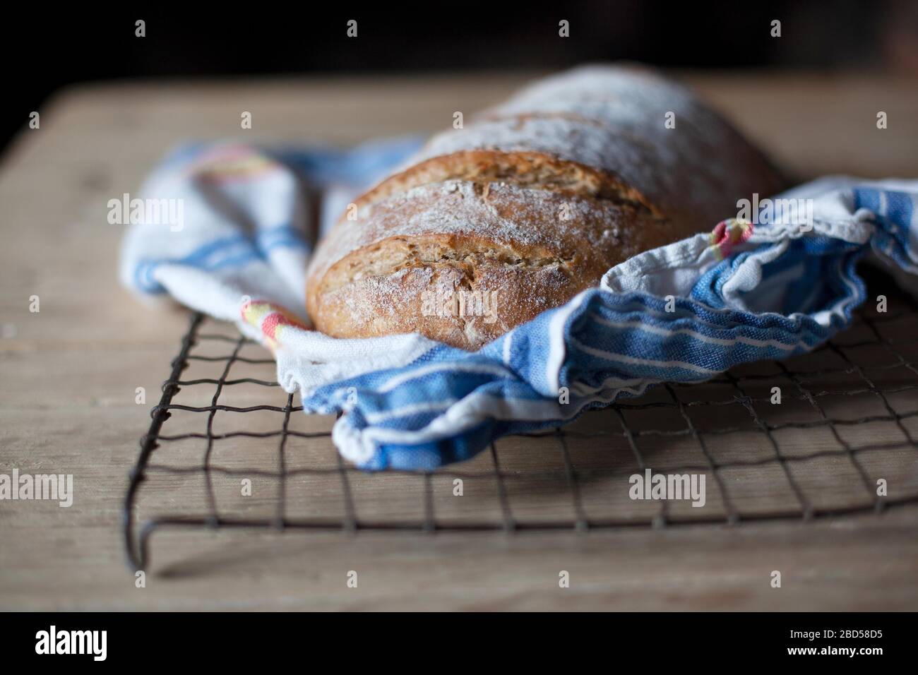 A freshly baked loaf of bread cooling on a wire rack on a wooden table Stock Photo