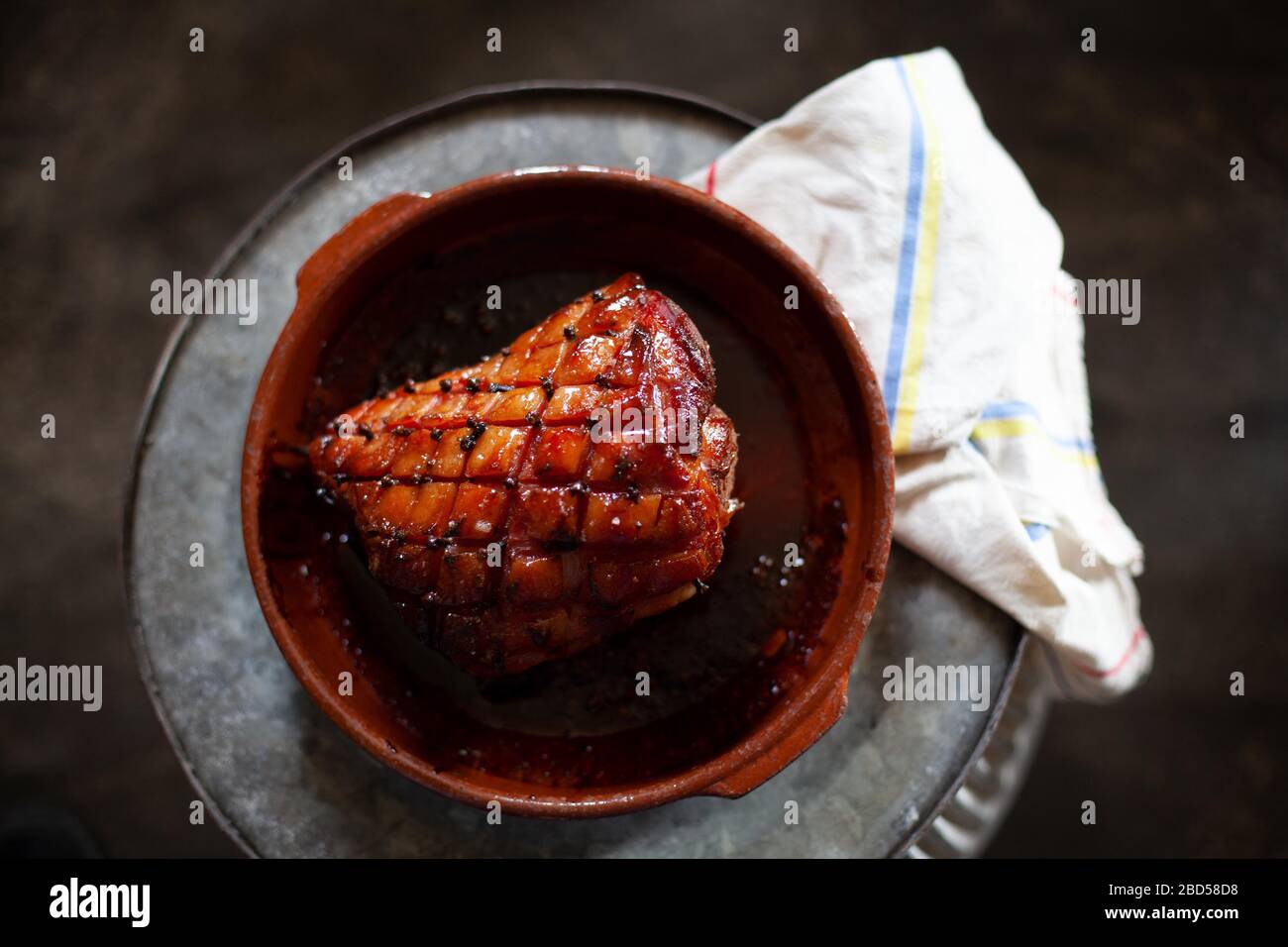 A roasted gammon joint in an earthenware dish on a dark background seasoned with cloves Stock Photo