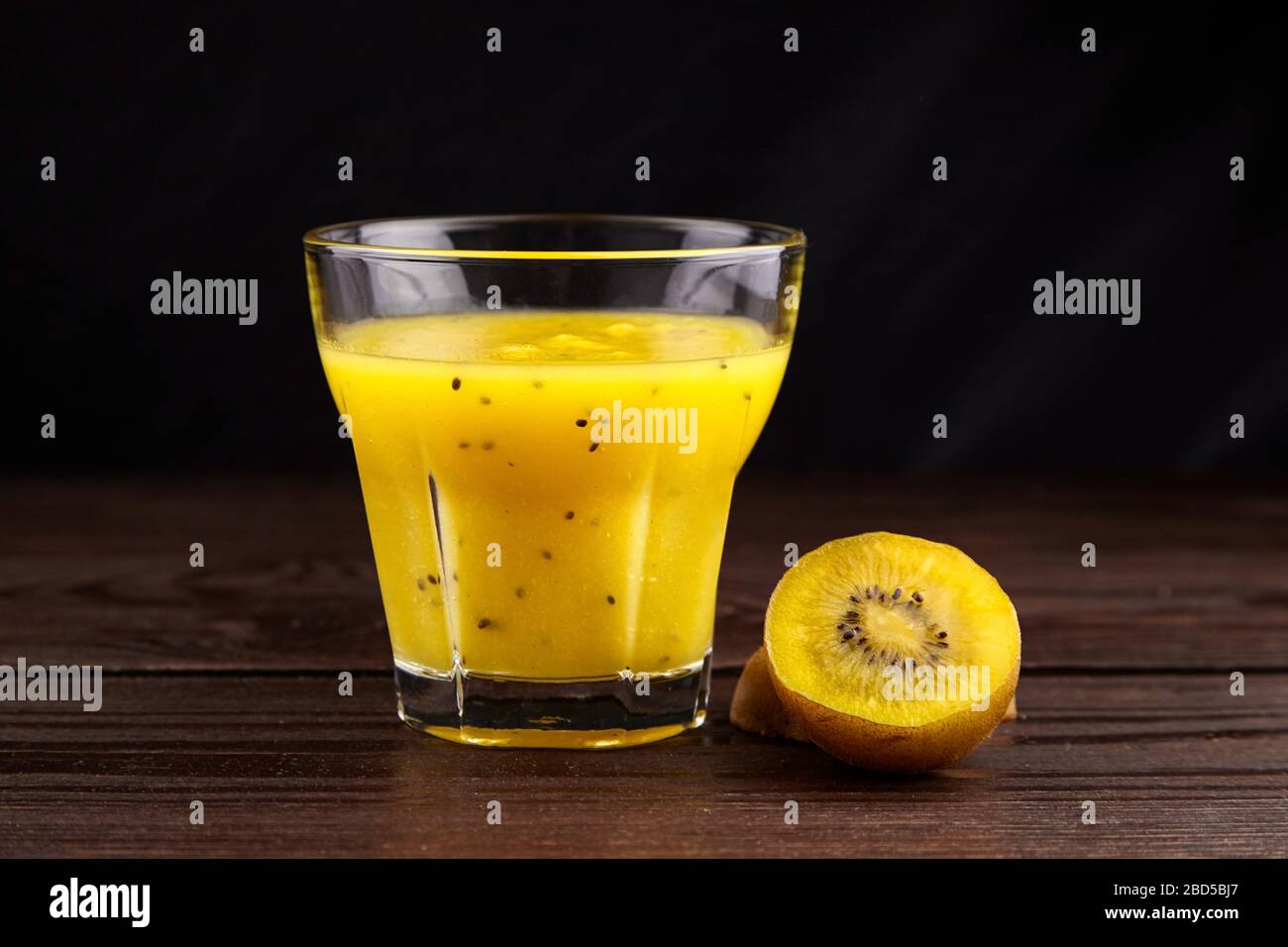 Kiwi gold fruit juice in transparent glass on wooden table on black background. Half of yellow kiwi. Fresh kiwi smoothie. Healthy food and drink Stock Photo