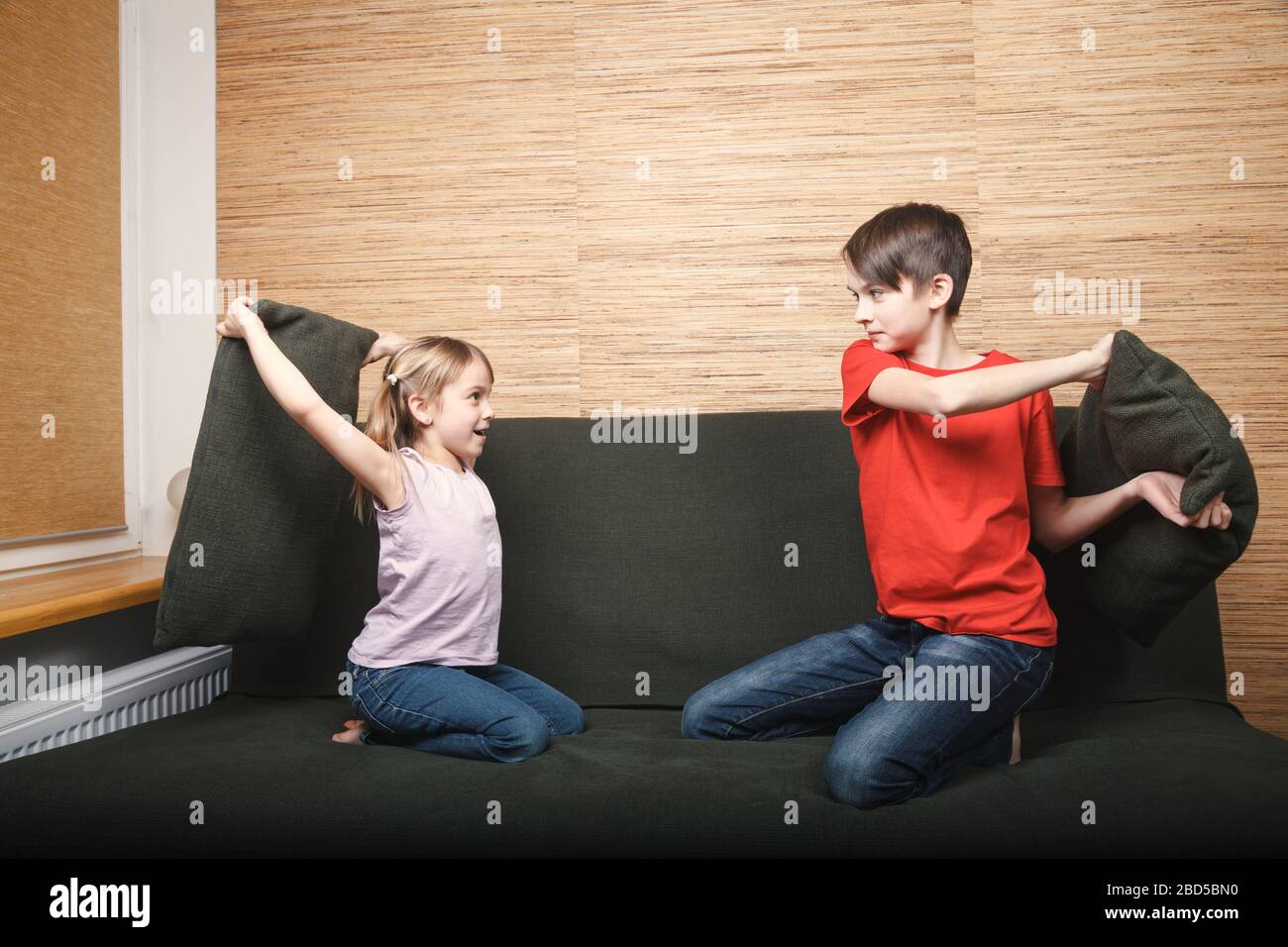 Siblings fighting with pillows stuck at home being in self-isolation. Quarantine and lockdown protective measures against spreading of coronavirus pan Stock Photo