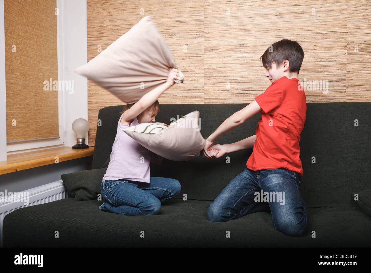 Siblings fighting with pillows stuck at home being in self-isolation. Quarantine and lockdown protective measures against spreading of coronavirus pan Stock Photo
