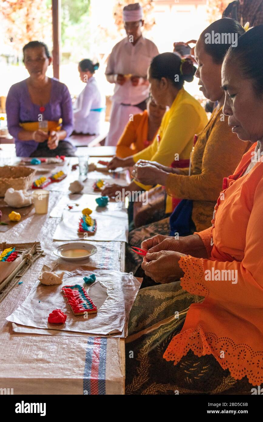 Vertical portrait of women and a holyman making religious decorations at a temple in Bali, Indonesia. Stock Photo