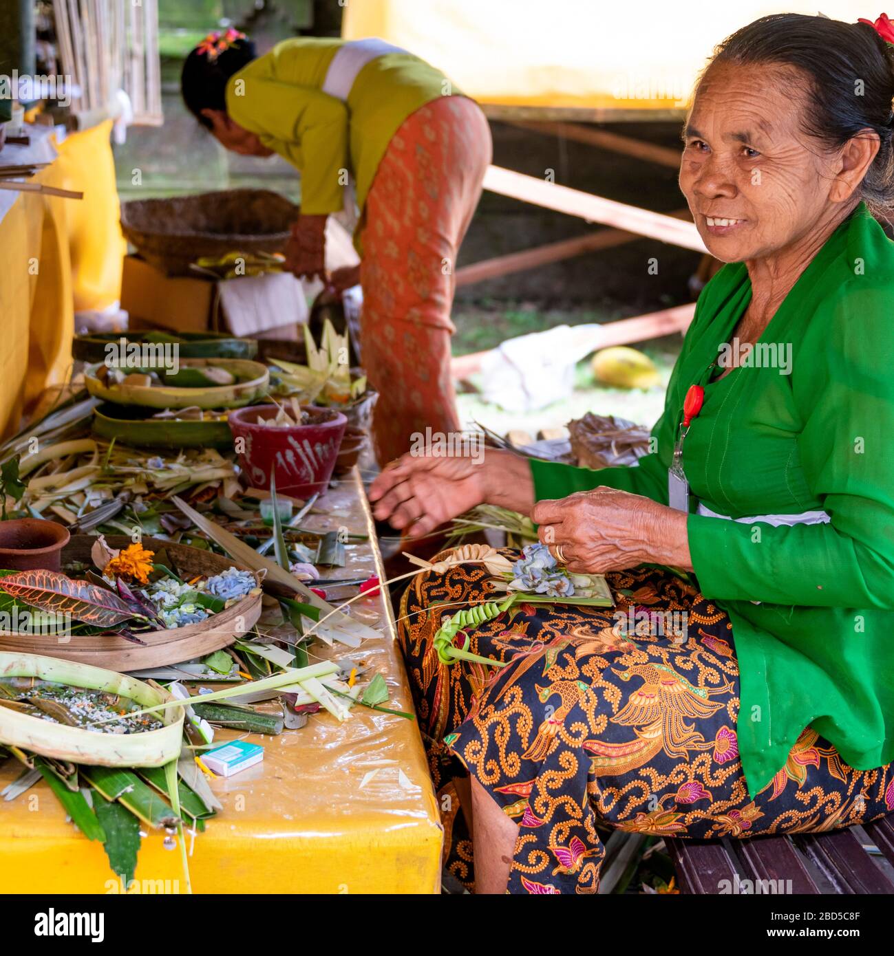 Square portrait of ladies weaving leaves into decorations at a temple in Bali, Indonesia. Stock Photo
