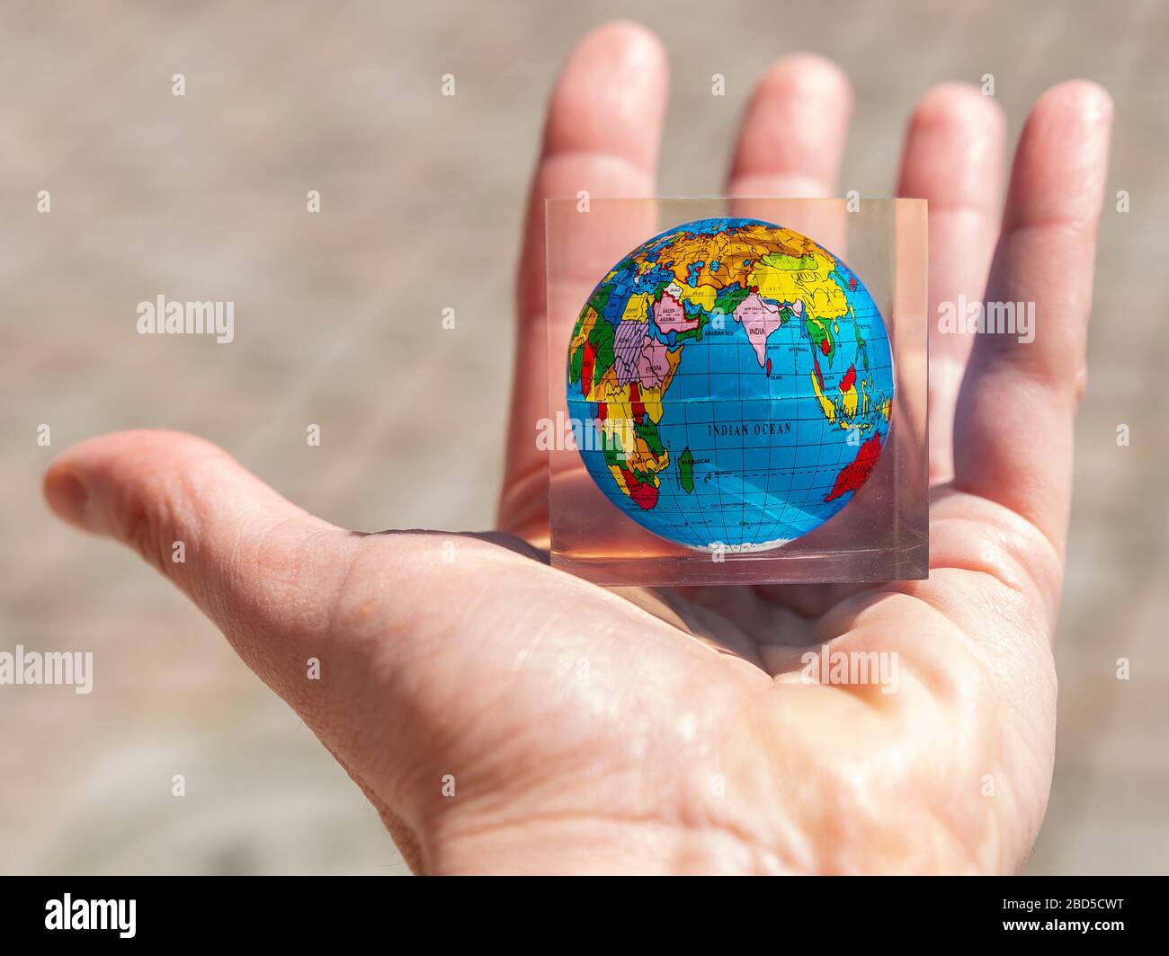 A male hand holds a colorful planet earth in the palm with a map in a transparent glass frame Stock Photo