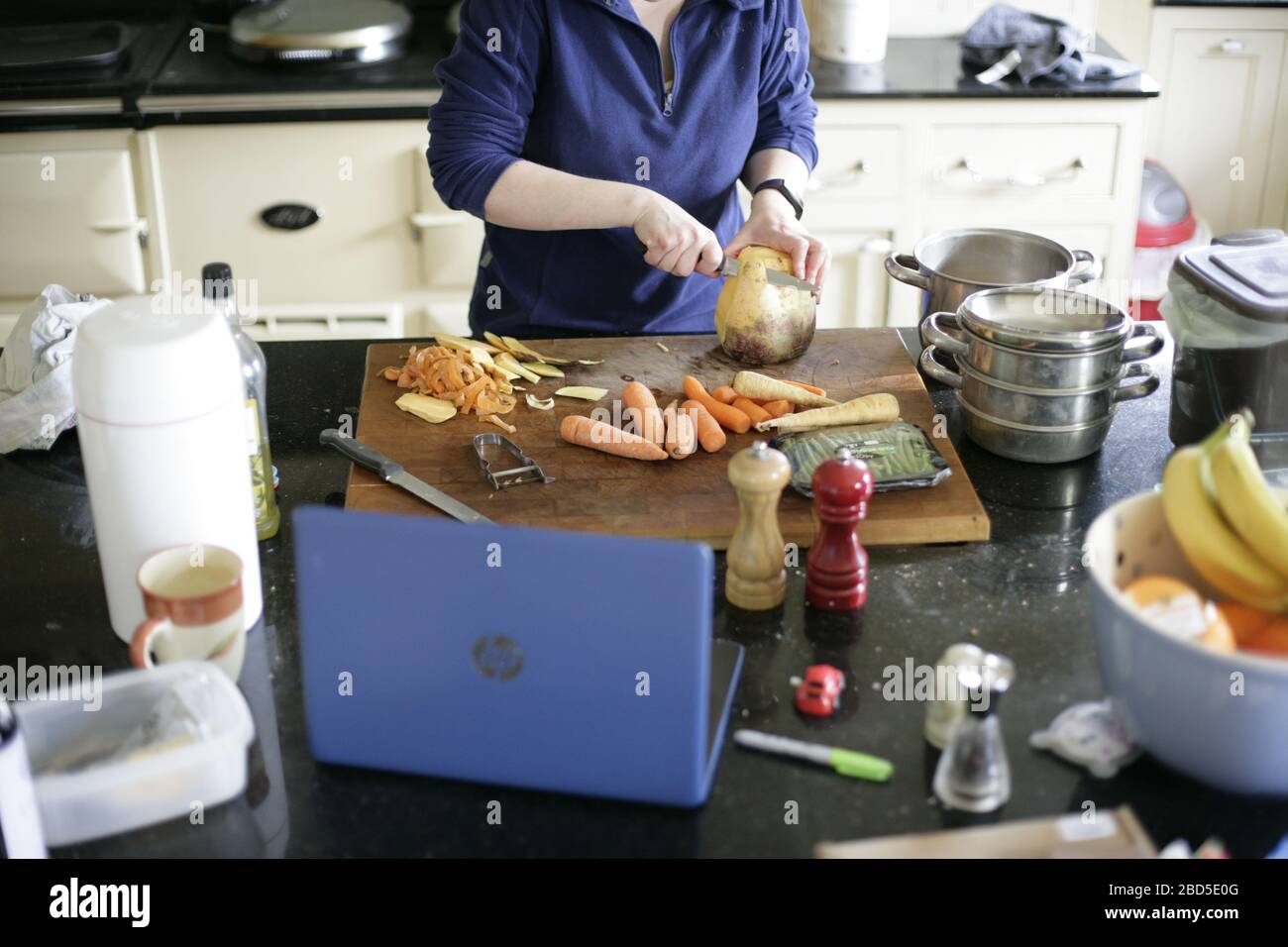 Mother preparing and cooking family dinner meals in kitchen whilst working from home during self-isolation - 2020 COVID-19 coronavirus pandemic Stock Photo