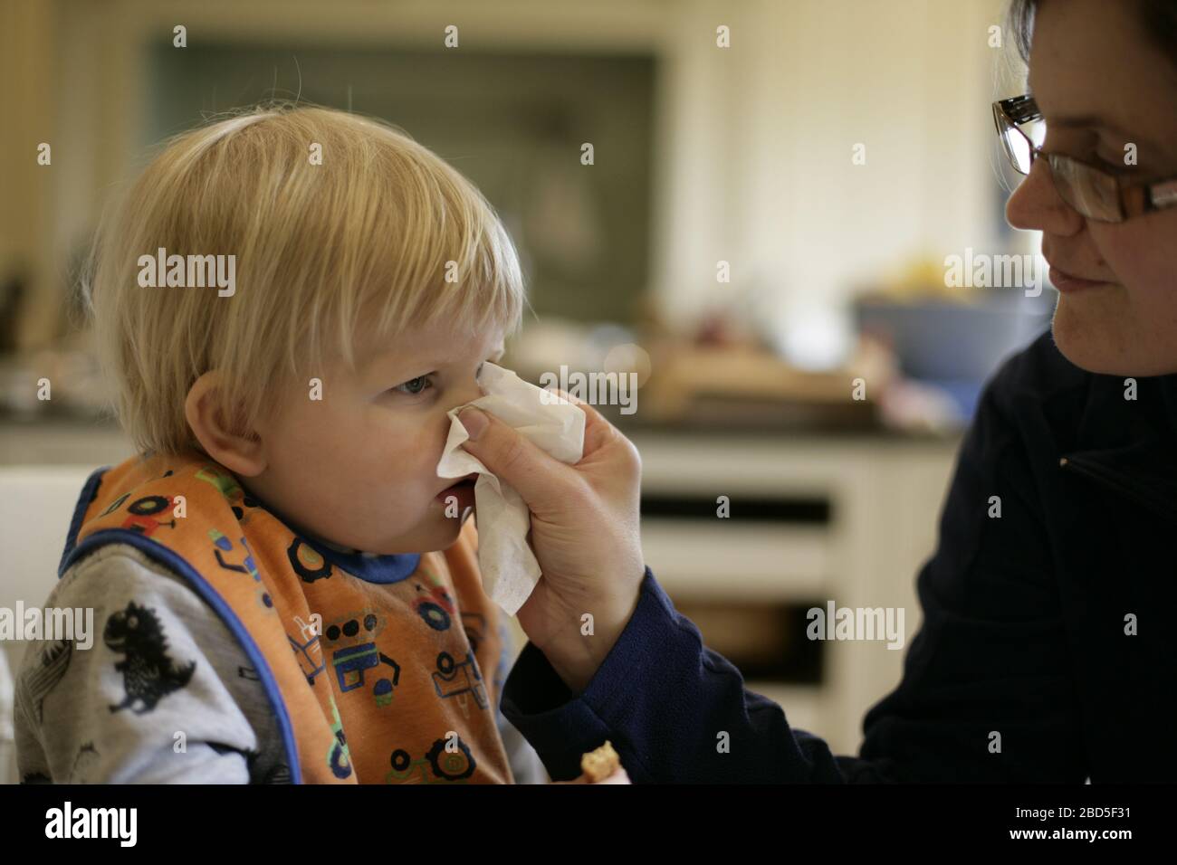Mother helping child toddler blow nose into tissue during period of self-isolating during the 2020 COVID-19 coronavirus pandemic Stock Photo