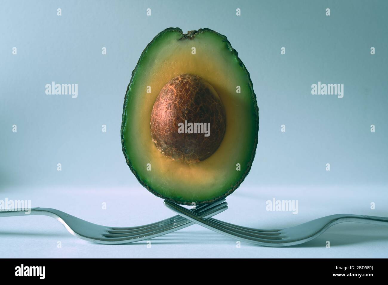 Avocado half balanced on forks with light blue background Stock Photo