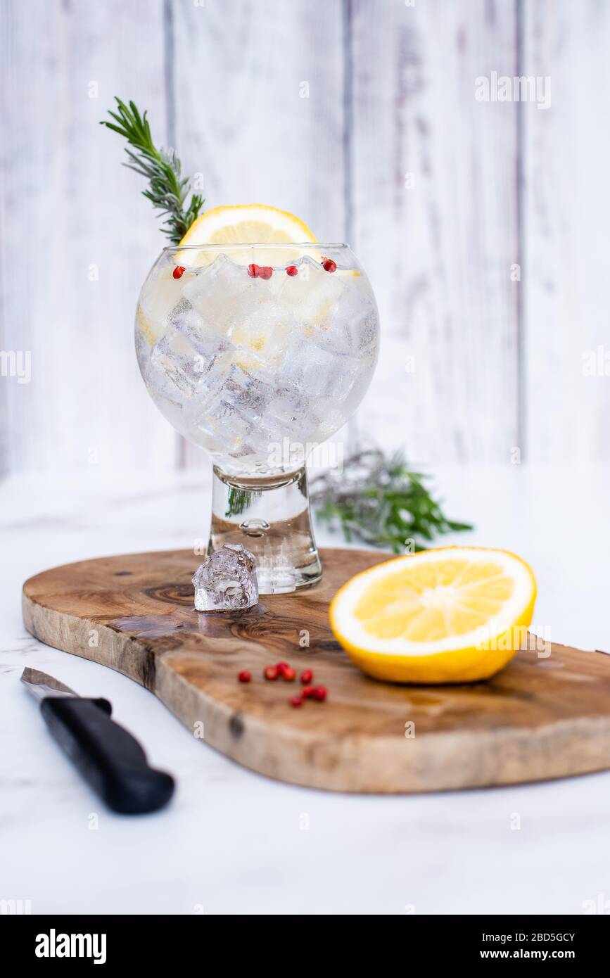 Cold Gin & Tonic cocktail with lemon garnish on wooden chopping board Stock Photo