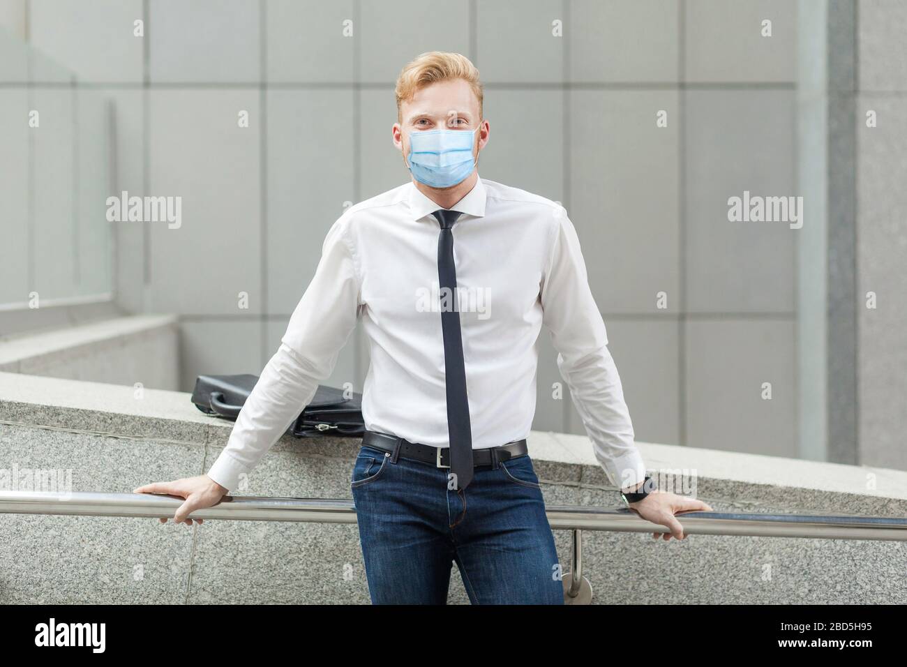Young successful businessman with surgical medical mask, in white shirt looking at camera satisfied. Outdoor shot in summer. business, working and hea Stock Photo