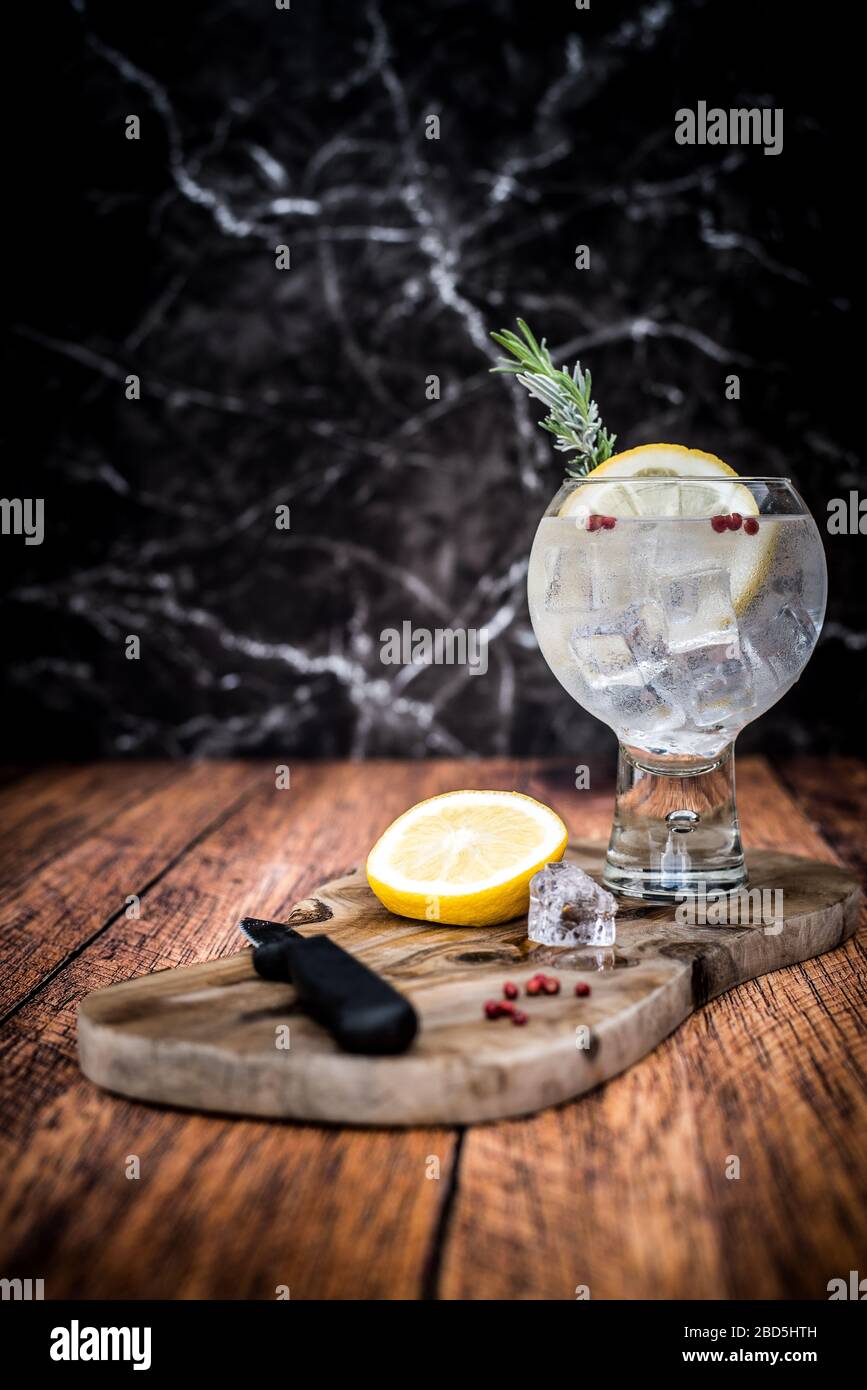 Cold Gin & Tonic cocktail with lemon garnish on wooden chopping board Stock Photo