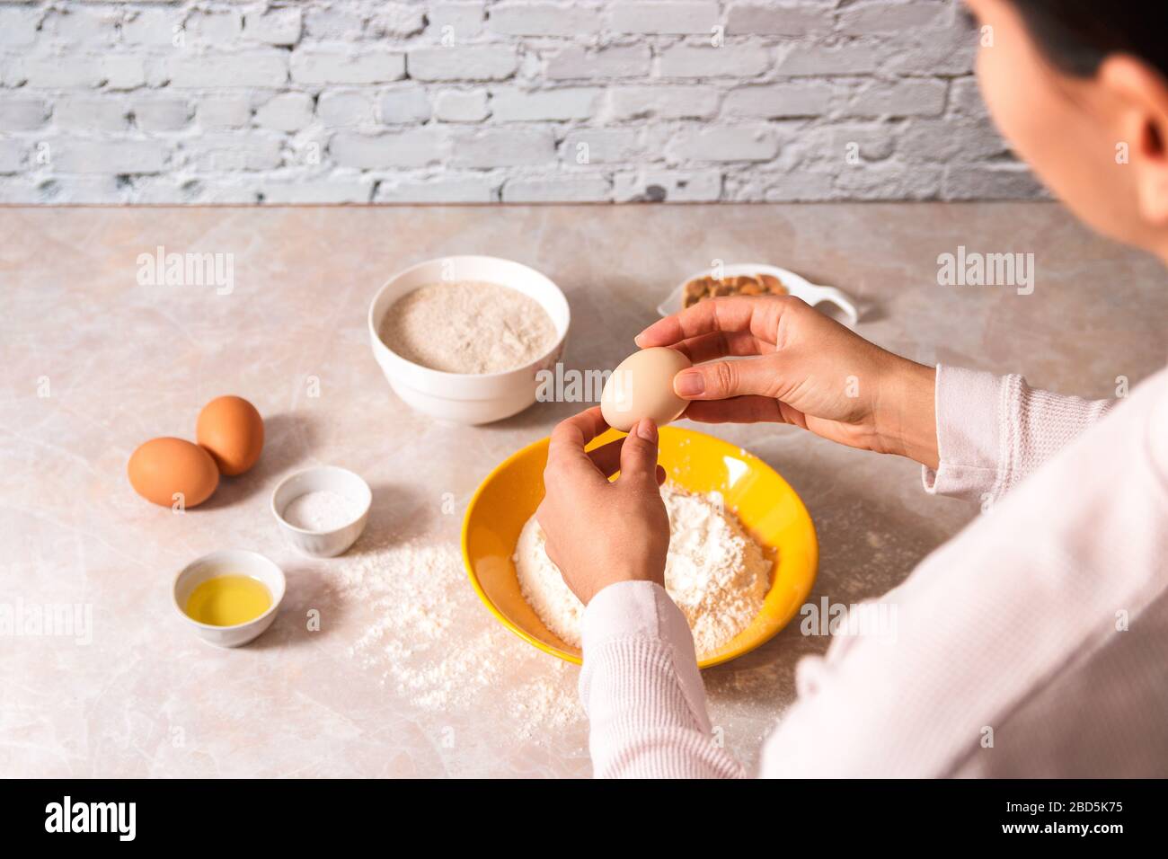 homemade bread baking. closeup woman hands adding egg in flour, dough