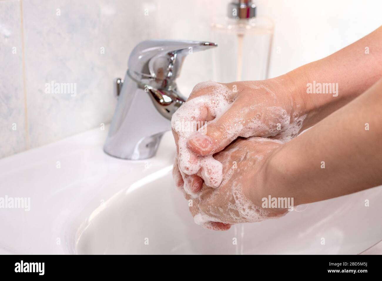 Woman using soap and hot water to wash her hands over a washbasin in a bathroom. Coronavirus pandemic prevention. Stock Photo
