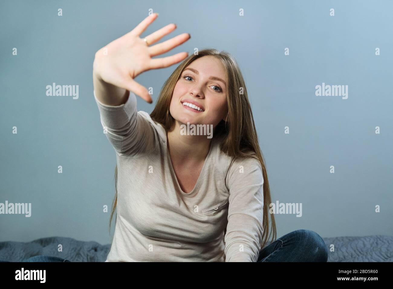 Portrait of young beautiful positive smiling woman waving her arm and looking at camera Stock Photo