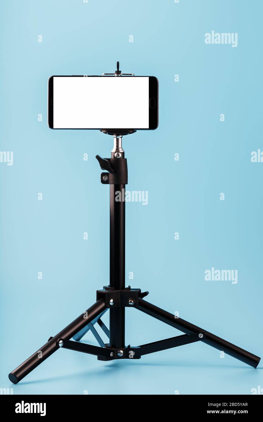 Mobile phone mounted on a tripod with a white display free for images and text, blue isolated background. Stock Photo