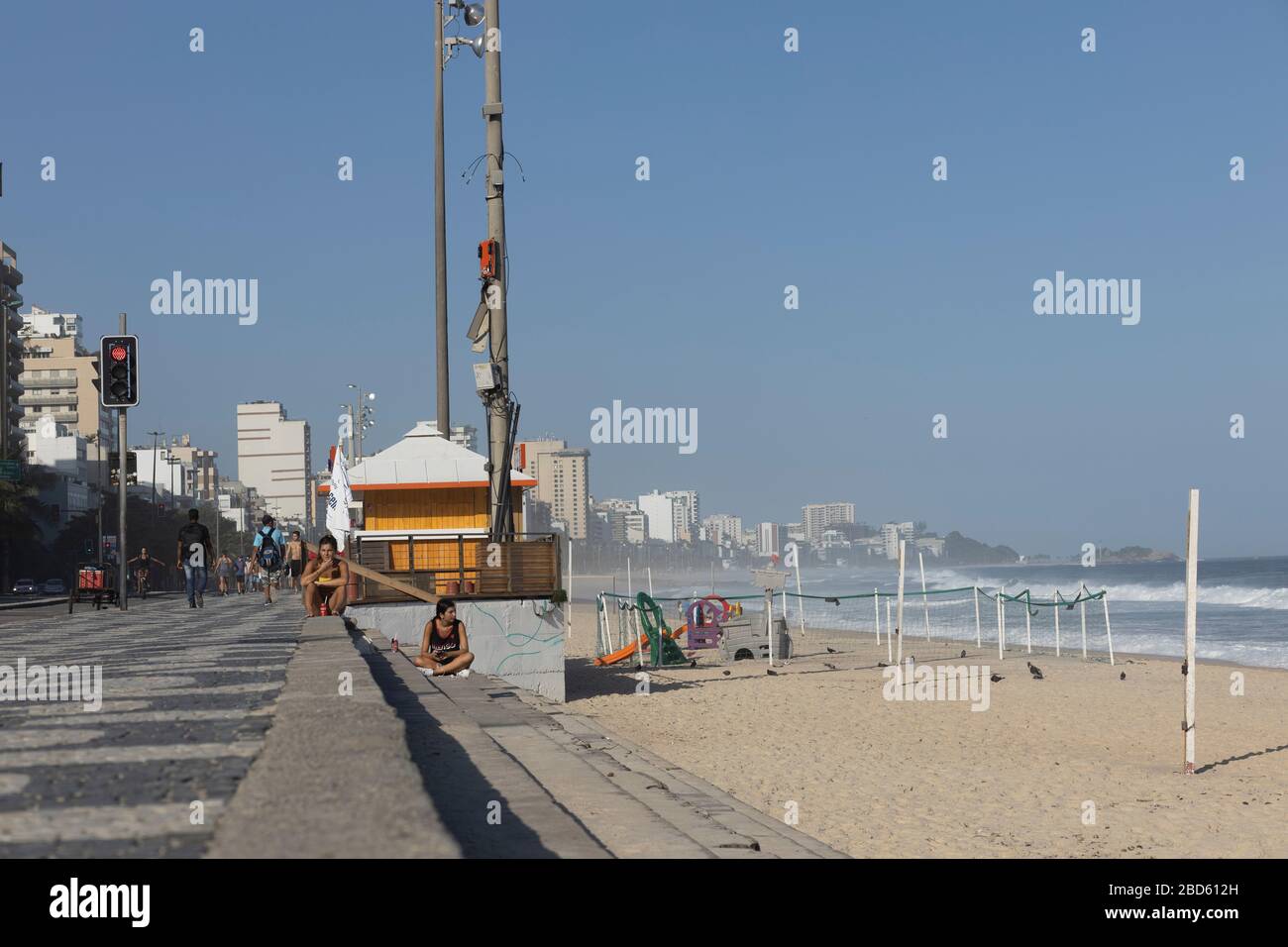 Leblon boulevard and beach during the COVID-19 Corona virus outbreak on a sunny midday with a closed kiosk and only a few people and little traffic Stock Photo
