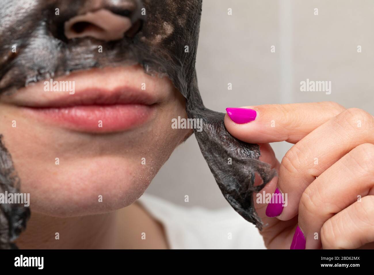 Close up picture of woman removing black charcoal peel off face mask from skin pore cleansing