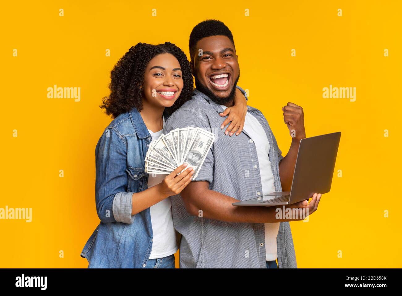 Sport betting. Excited african couple with bunch of dollars and laptop Stock Photo
