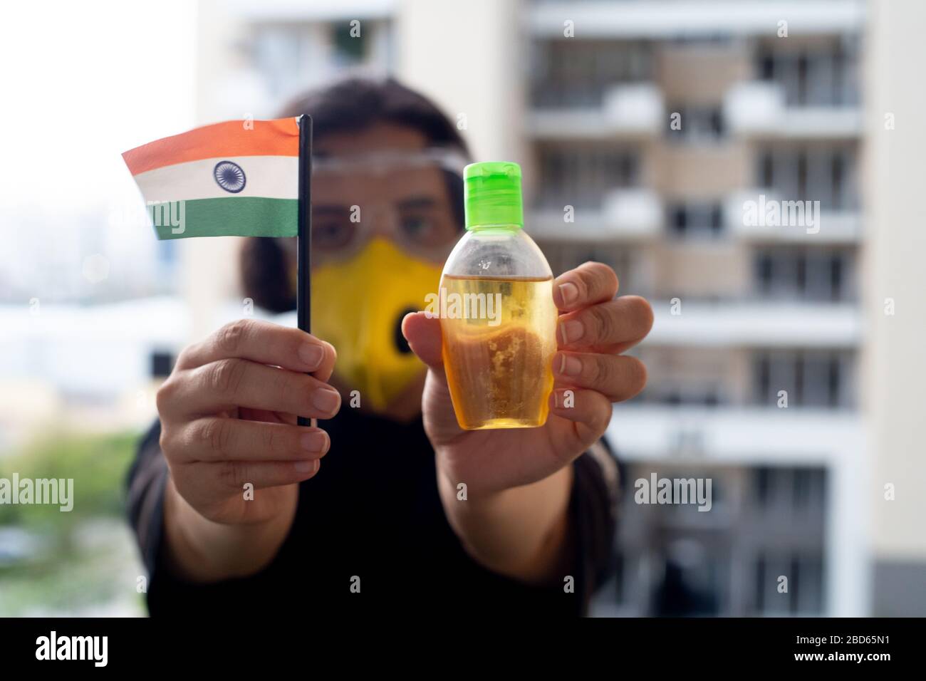 Young indian girl in mask and goggles holding an indian flag and sanitizer to stay safe during the current coronavirus pandemic Stock Photo