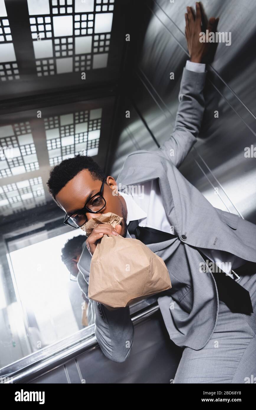 stressed african american businessman breathing with paper bag and suffering from panic attack in elevator Stock Photo