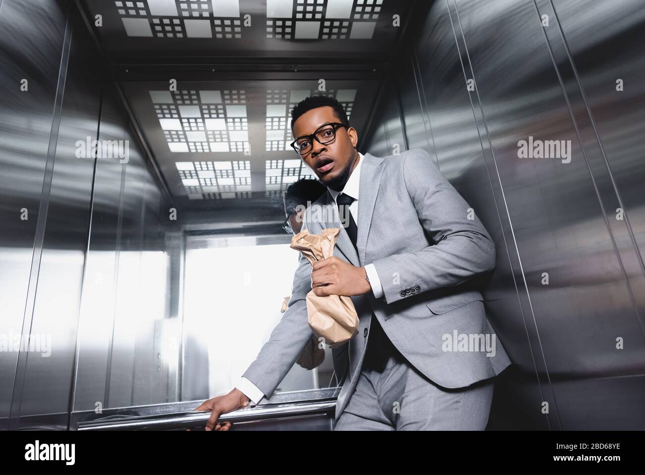 nervous african american businessman with paper bag suffering from panic attack in elevator Stock Photo