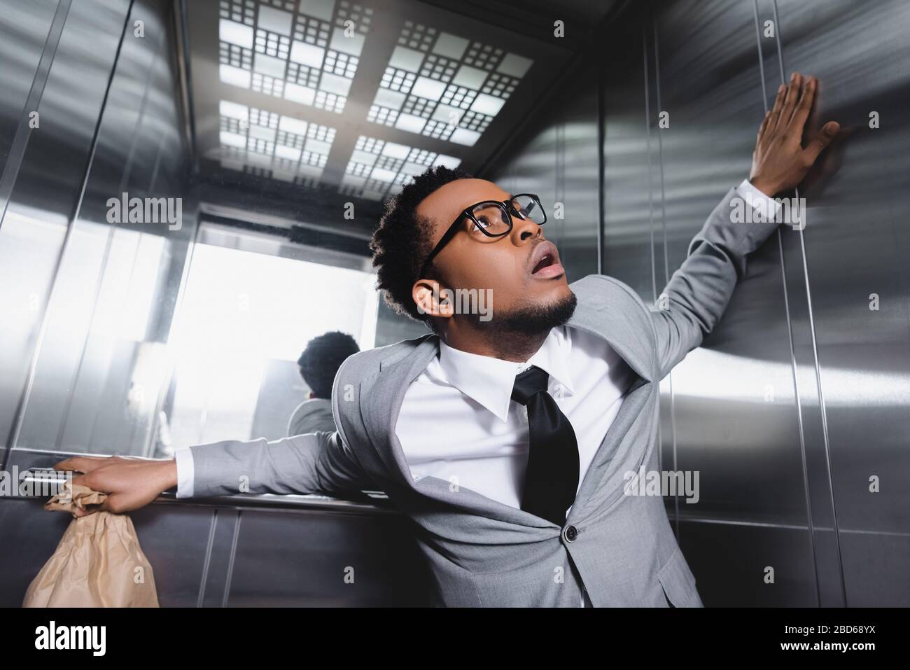 scared african american businessman with paper bag suffering from panic attack in elevator Stock Photo