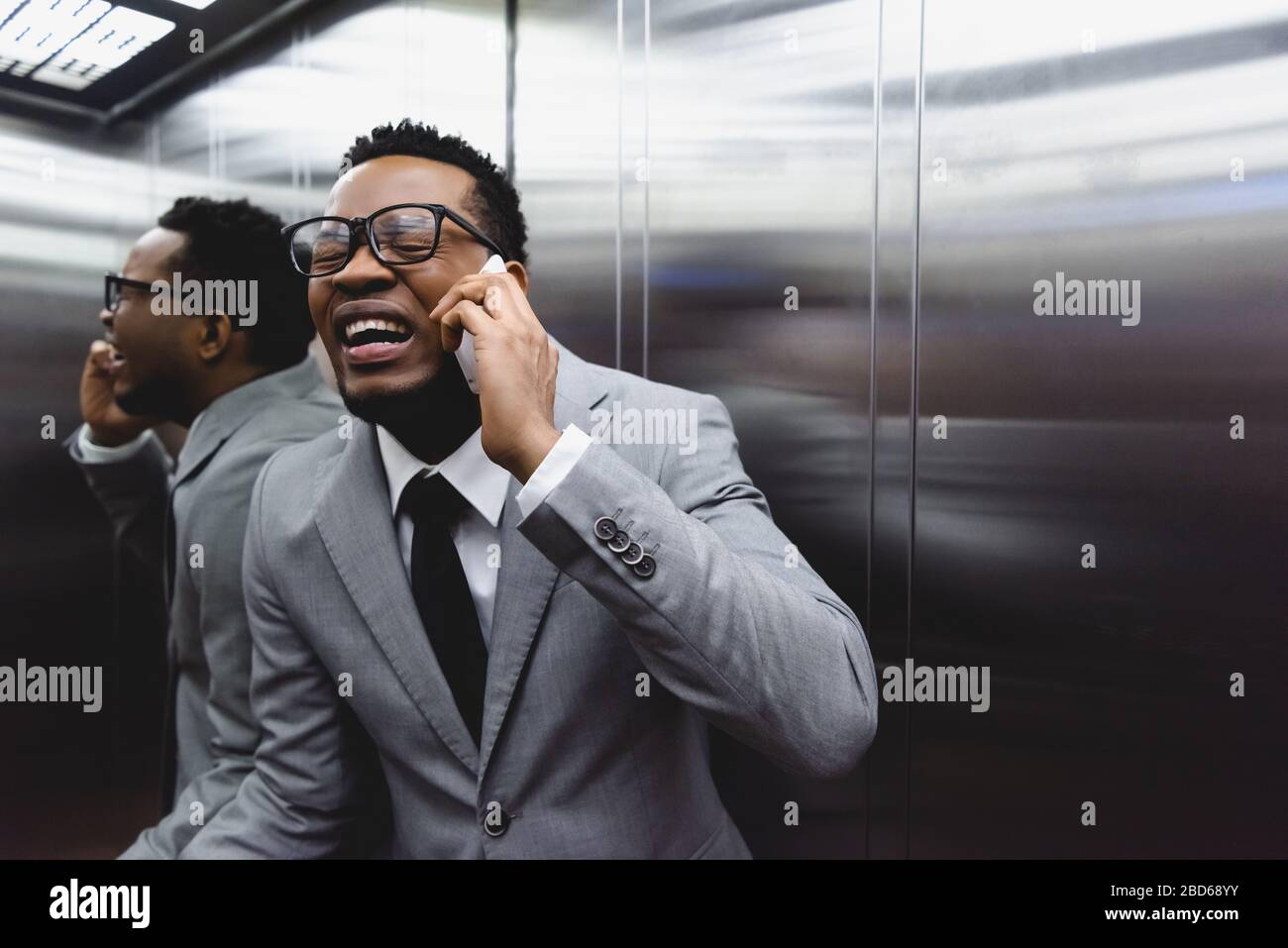 crying african american businessman talking on smartphone and suffering from panic attack in elevator Stock Photo