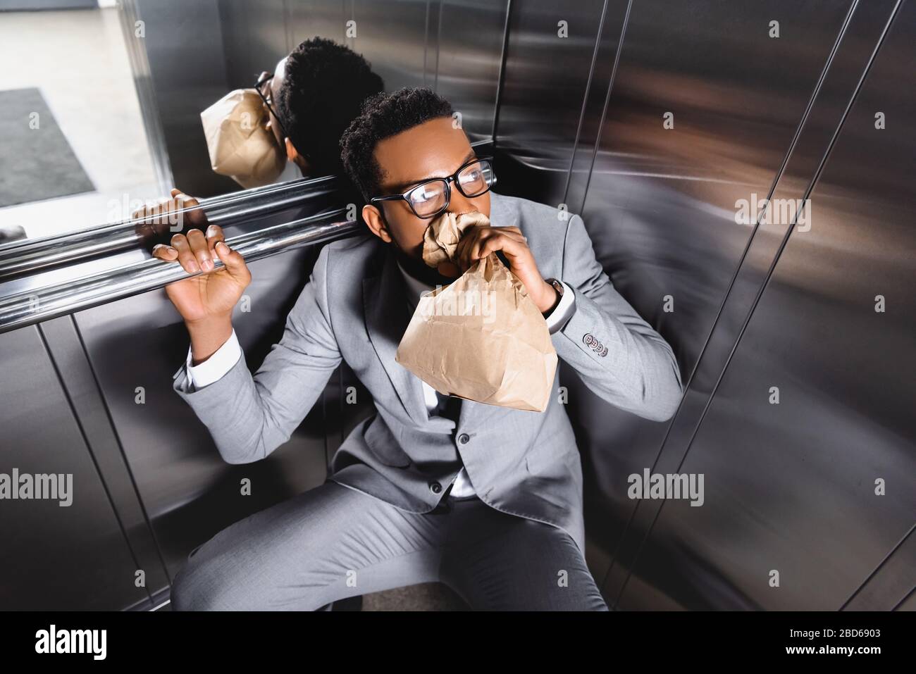scared african american businessman breathing with paper bag and suffering from panic attack in elevator Stock Photo