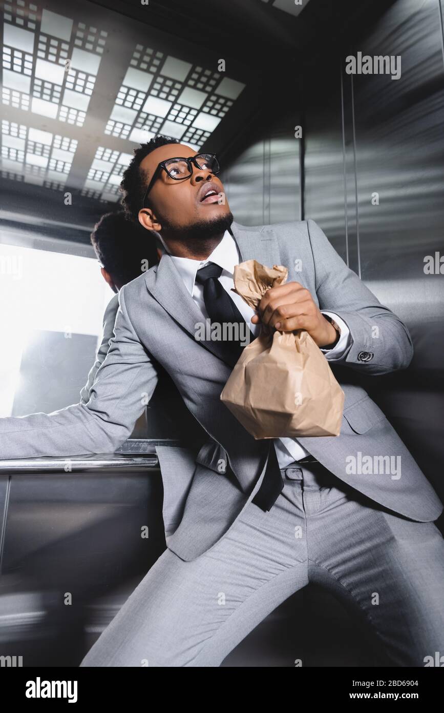 scared african american businessman with paper bag suffering from panic attack in elevator Stock Photo