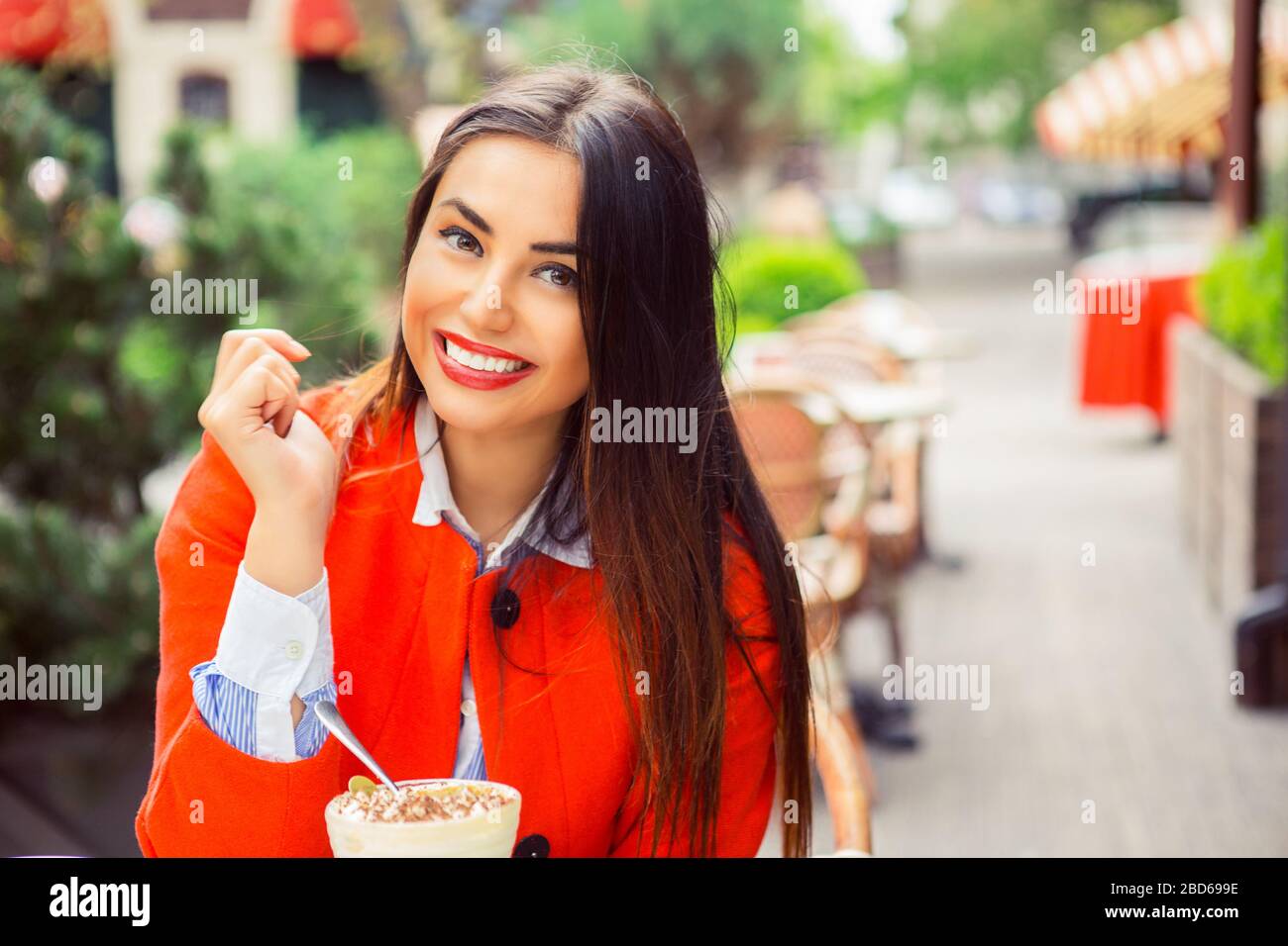 Cheerful cute young Indian woman smiling happy sitting and drinking cocktail on a outdoor cafe terrace balcony Stock Photo