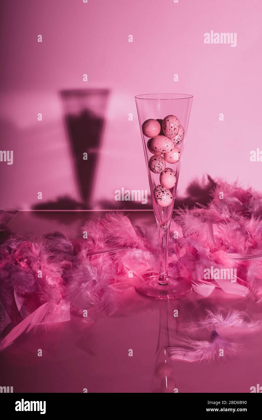 Quail eggs in champagne flute with feathers on glossy background. Creative still life in pink color. Easter concept. Stock Photo