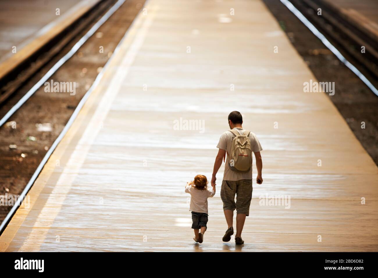 Father holds is toddler's hand as they walk along a platform between