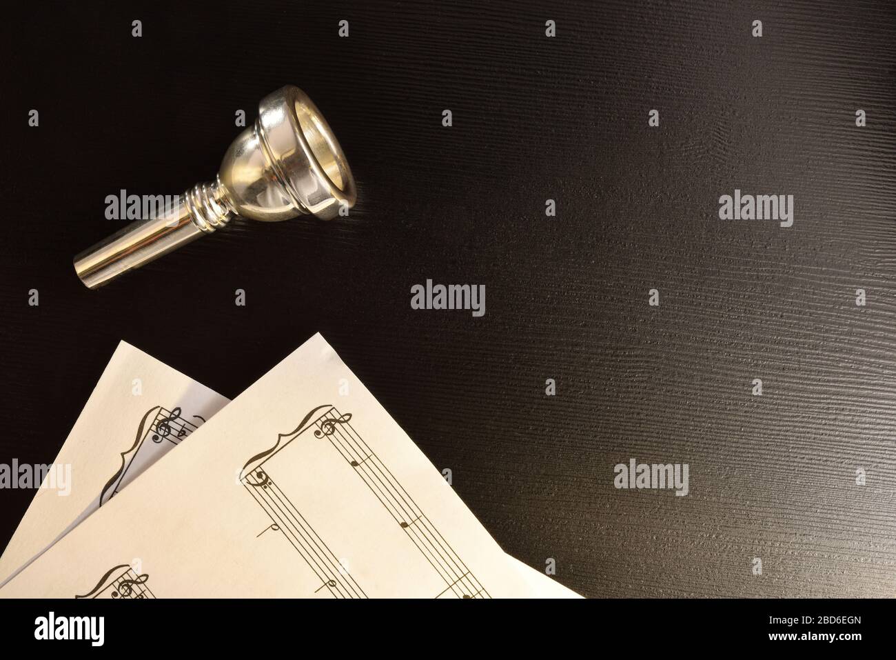Mouthpiece of metal musical instrument and scores on black table. Top