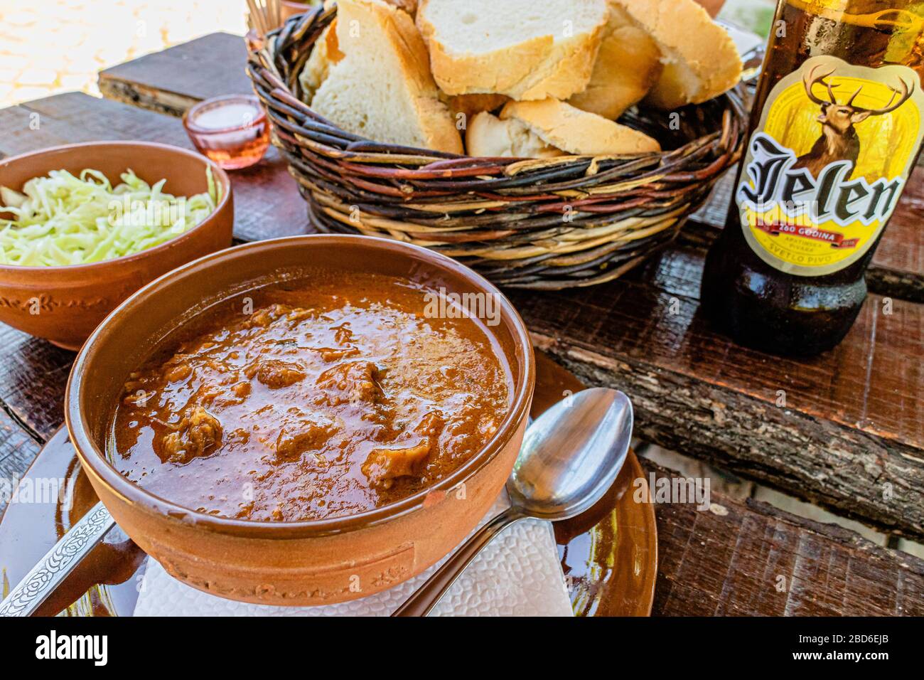 Traditional beef goulash served with bread, onions and a bottle of Jelen beer, from a cafe at Zasavica nature park, Serbia. May 2017. Stock Photo