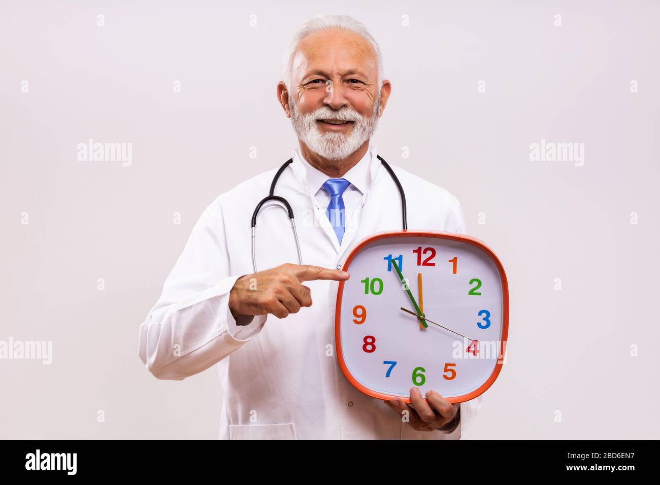 Portrait of senior doctor holding clock on gray background. Stock Photo