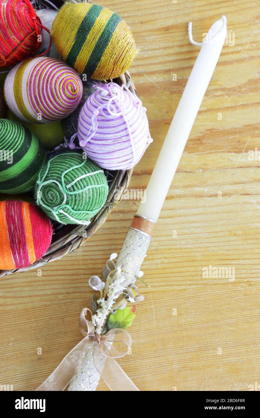 Eggs decorated with threads an Easter candle beside on wooden table Stock Photo