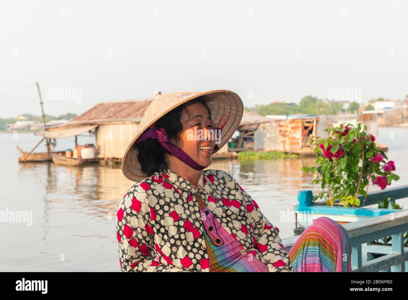 Smiling Vietnamese woman living on a floating house and wearing a traditional conical hat on the Mekong Delta, Vietnam, Southeast Asia Stock Photo