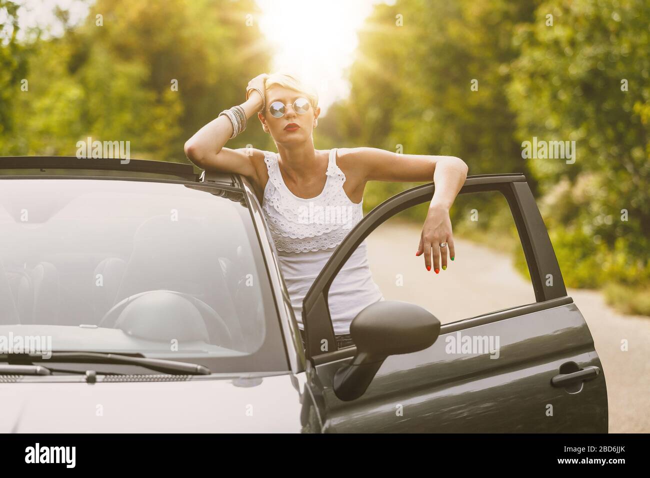 Young blonde attractive woman is ready to enter in her car. She is opening the door and staying behind it. Stock Photo