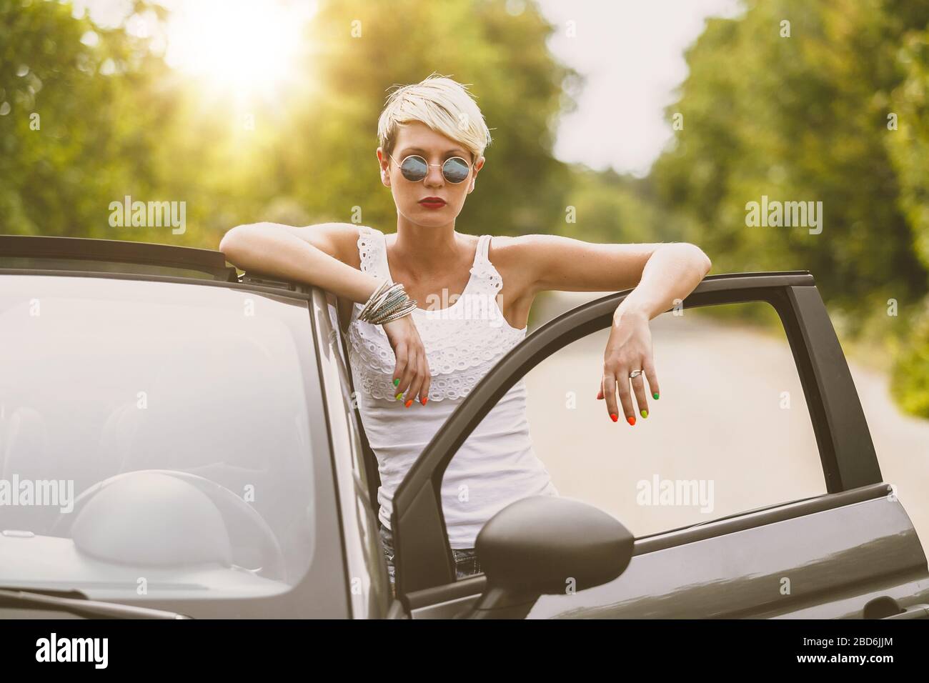 Young blonde attractive woman is ready to enter in her car. She is opening the door and staying behind it. Stock Photo